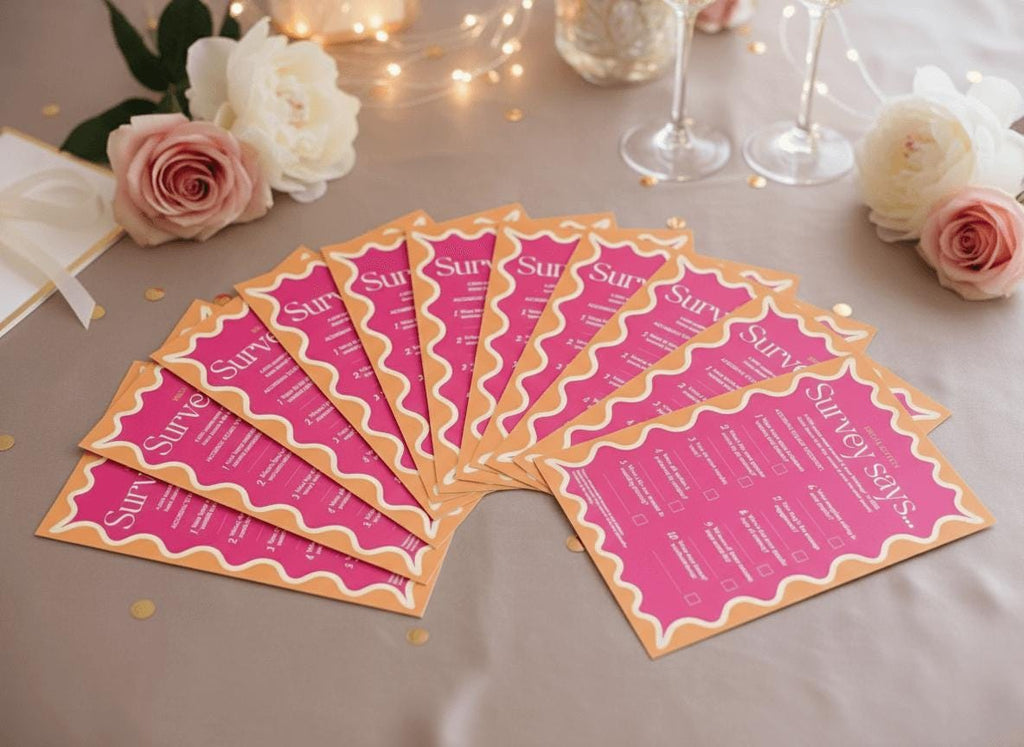 Multiple bridal family feud game cards on a surface with roses and tea lights and champagne flutes.