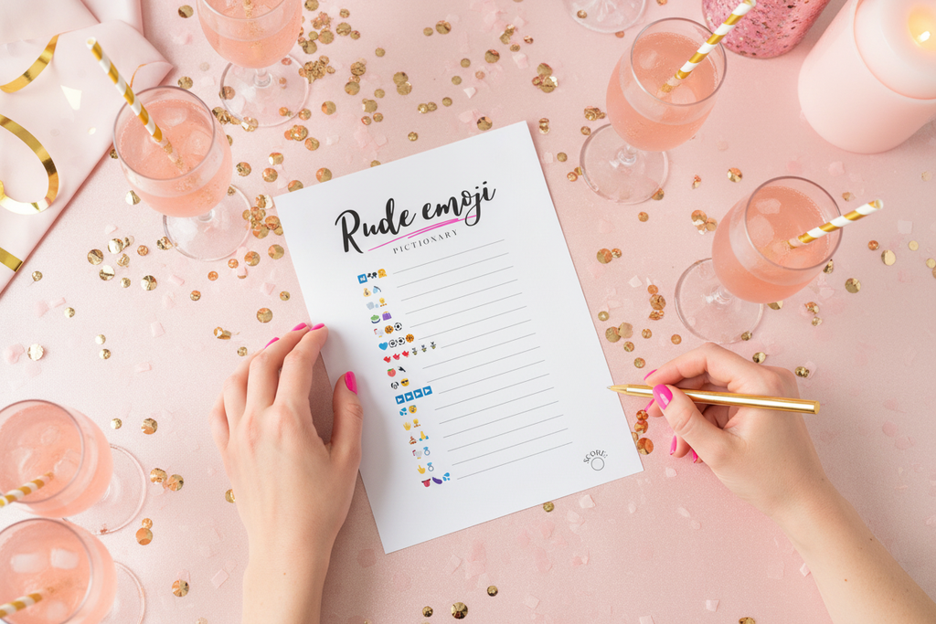 Rude emoji pictionary naughty bachelorette game on pink table with confetti and two hands.